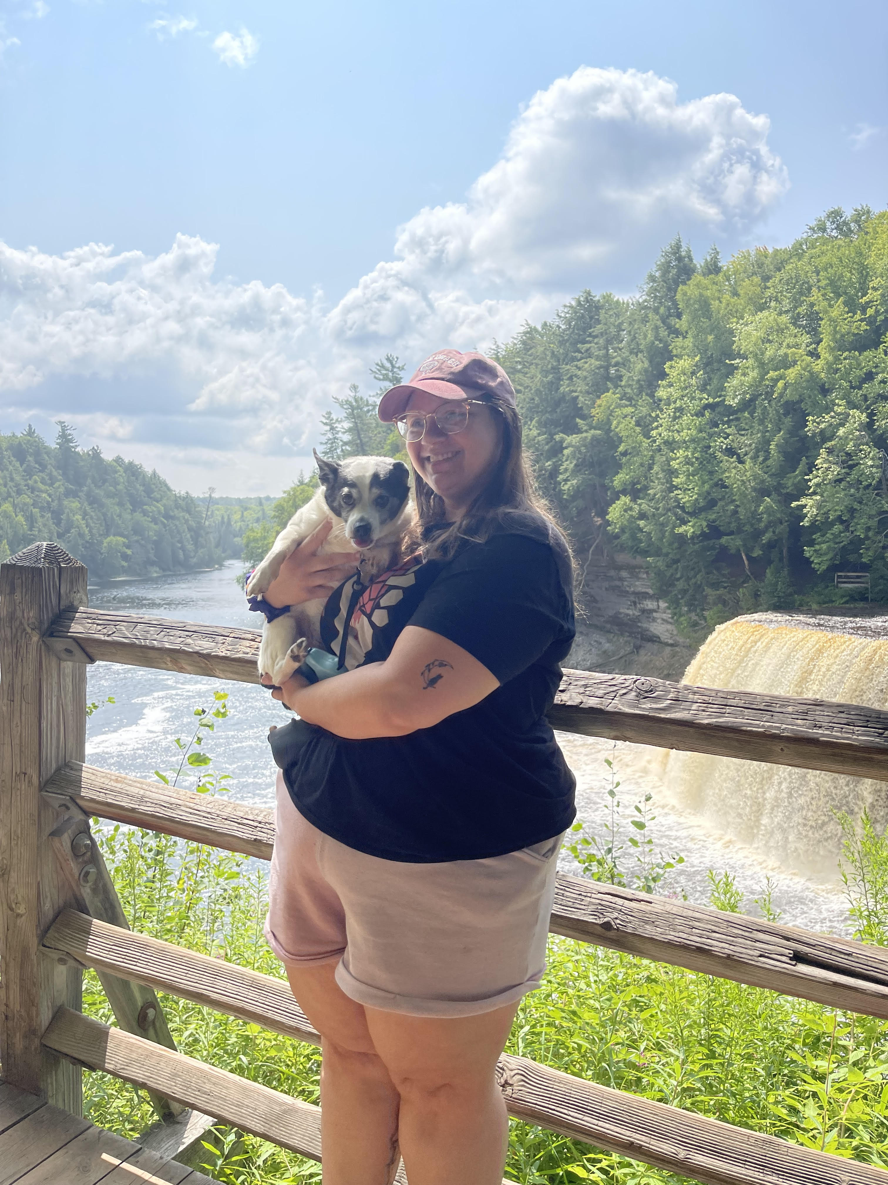 small black and white dog being held by a woman infront of a waterfall.